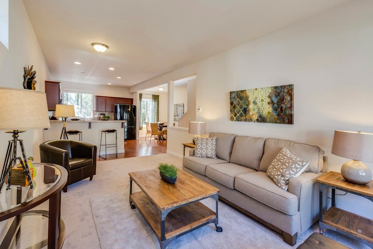 A sunlit living room with a neutral sofa, wooden coffee table and open kitchen